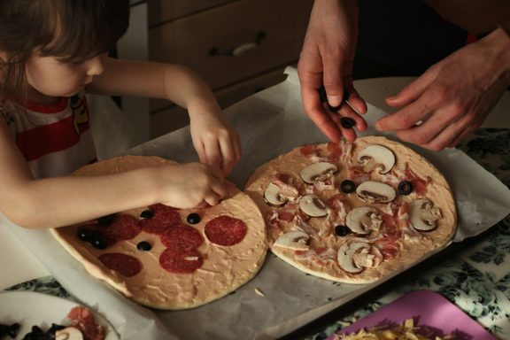 A child and an adult putting toppings on their home-made pizzas.