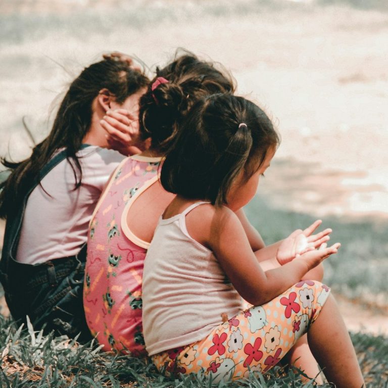 Three children sitting together on a grass field.